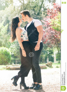 Beautiful couple embrace and love. Loving relationship and feeling. A men and a women is strongly embrace with passion and feeling. Love affair between two young people. Behind them a natural park with trees and colorful foliage. Bright light that illuminates the scene.