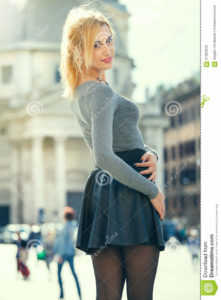 Blonde girl in the town, happily young tourist woman A beautiful young girl walks in the historic center of Rome in Italy. She is smiling, her look is trendy. Bright day and historical buildings in the background. Skirt and stockings.