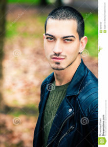 Handsome young man outdoors, short hair style A handsome boy outdoors. Eyes with intense look and stylish hair. Behind him one winter autumn scenery. The young man wearing a leather jacket rock style.