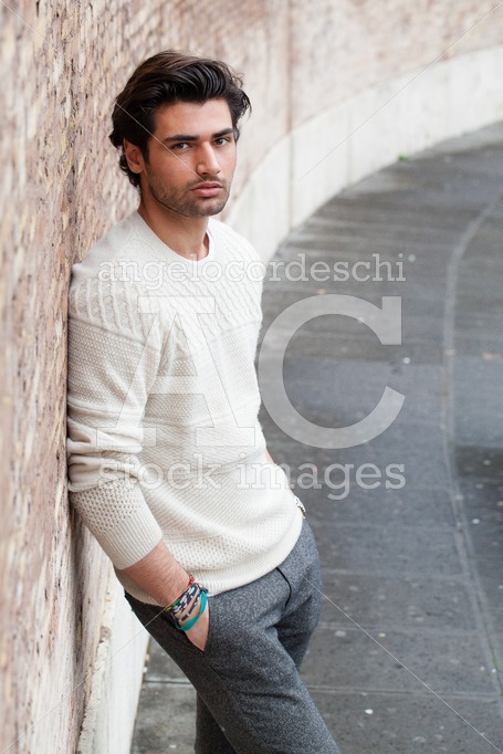 Handsome Young Man Leaning On A Long Wall Outdoors, Hands In His Angelo Cordeschi