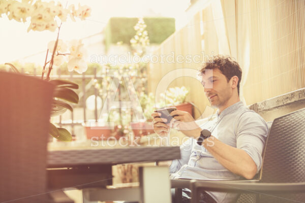 Outdoor Man Sitting And Relaxed Texting With A Smartphone In His Angelo Cordeschi